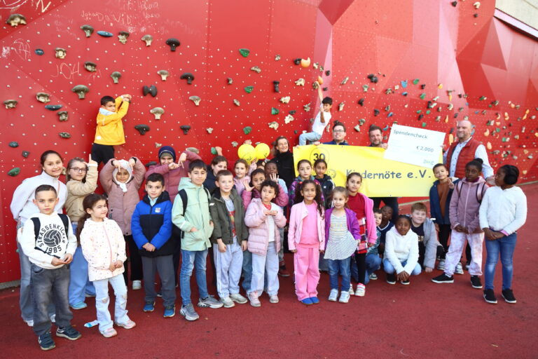 Kinder, Vertreter von <span class=knstyle>Kindernöte e.V.</span> und vom IKEA-Team Butzweilerhof mit Spendenscheck vor einer Kletterwand in Chorweiler