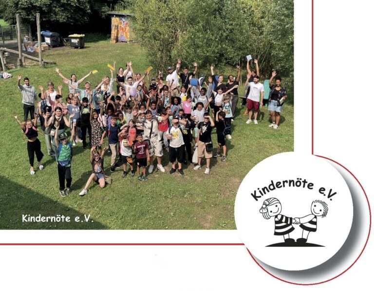 Gruppenfoto: viele Kinder und Betreuer jubeln mit erhobenen Armen auf einer Wiese, daneben das Vereinslogo